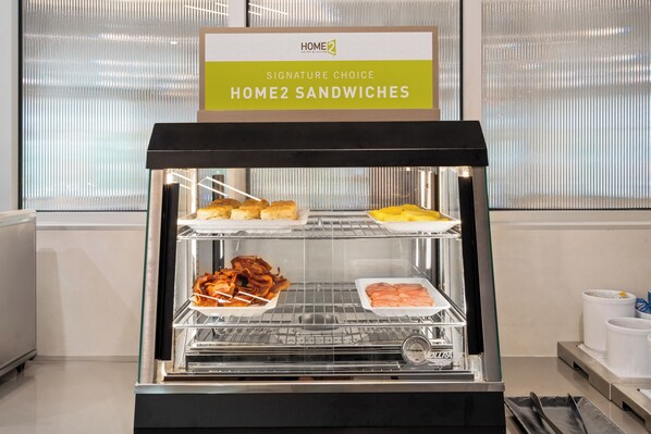A food display with sandwiches and bacon, labeled 'Signature Choice Home2 Sandwiches'.