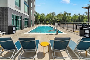 A swimming pool with lounge chairs and tables, surrounded by a fence and trees.