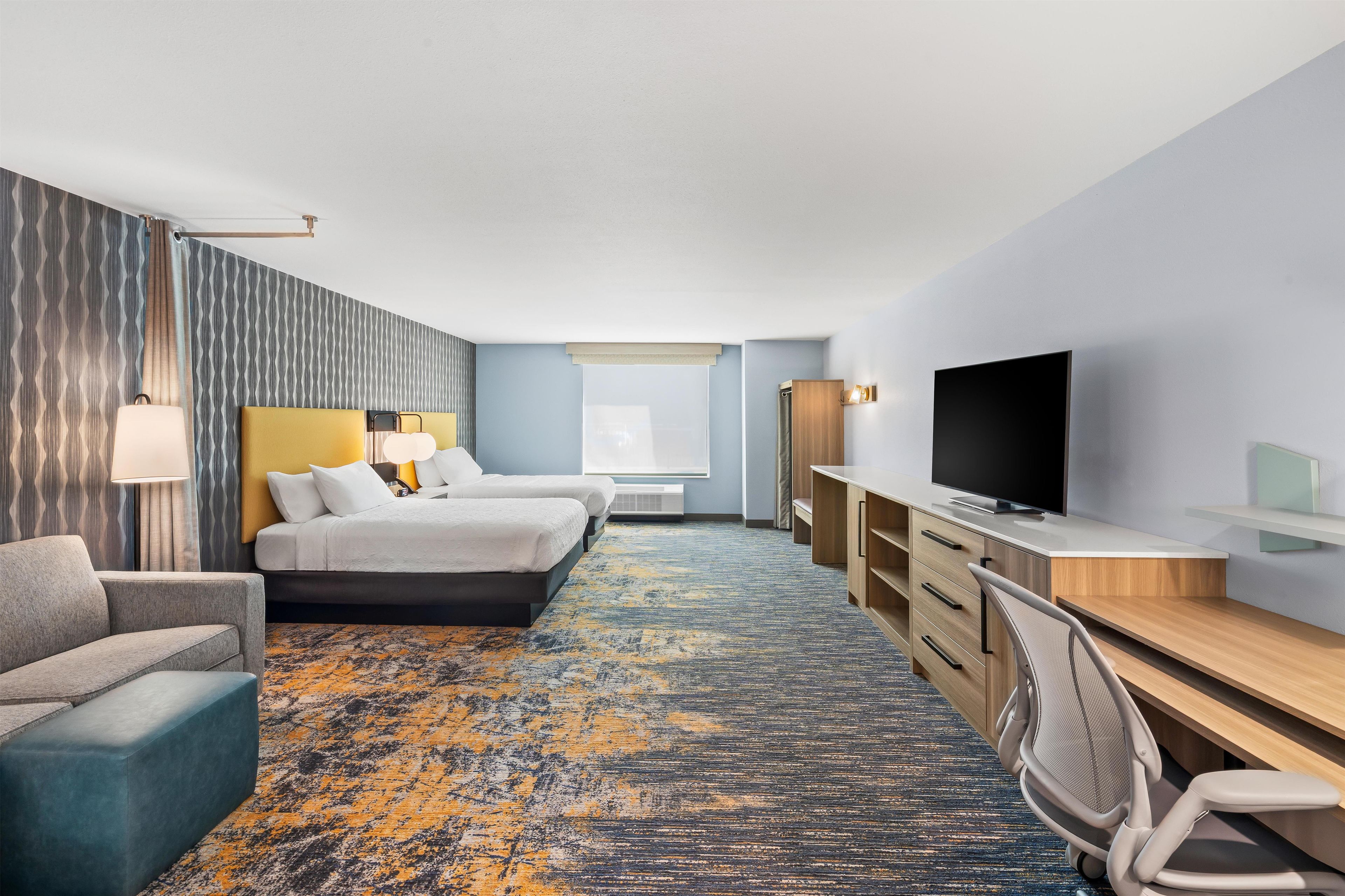 A hotel room with a bed, a desk, a TV, a chair, and a couch.