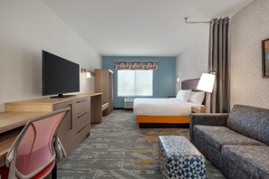 Una camera d'albergo con un letto, una scrivania con televisore, una sedia, un divano e un tappeto decorato.