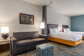 Een hotelkamer met een slaapbank, een bed, een nachtkastje, een lamp en een kamerkleed met dessin.