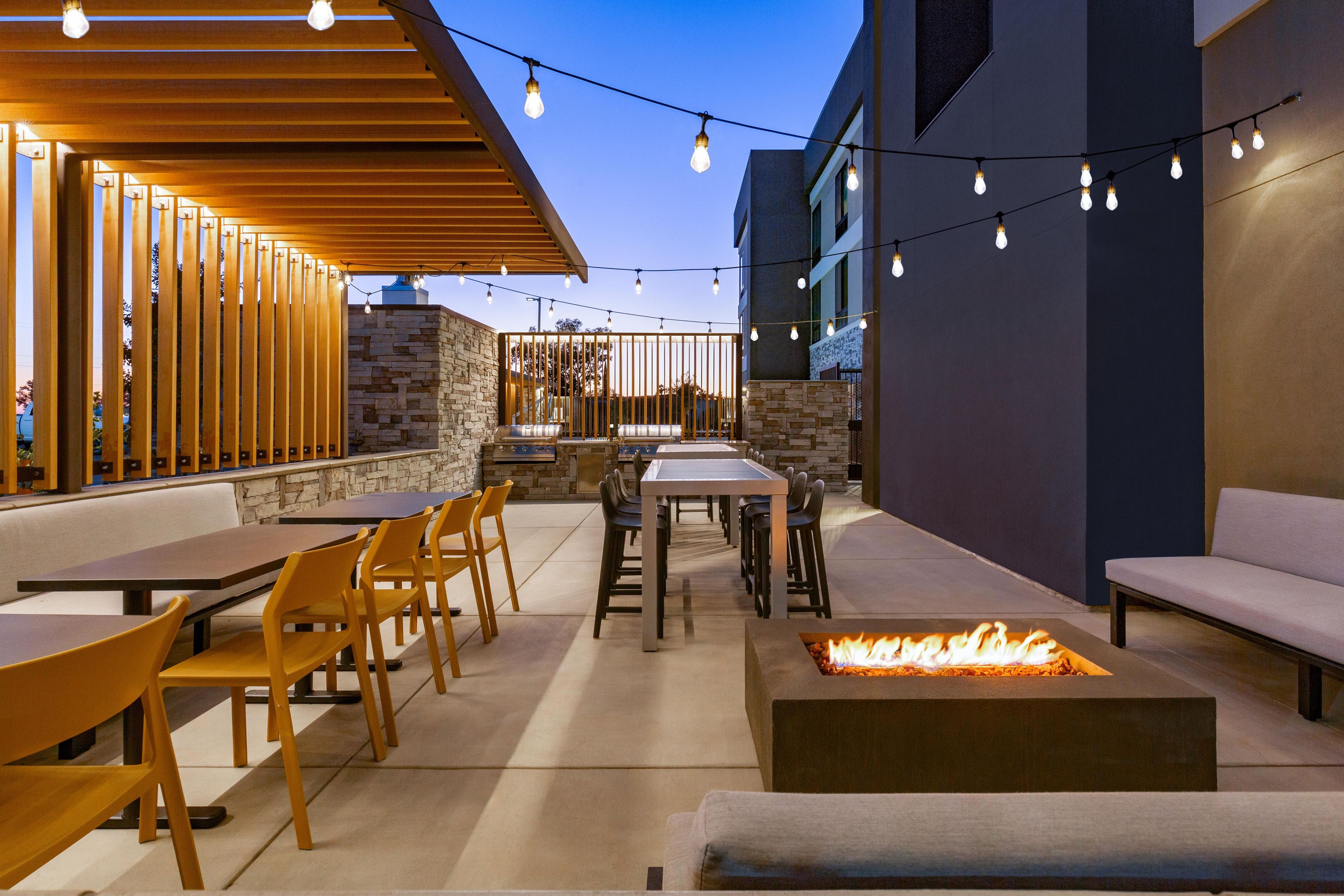 An outdoor patio area with tables and chairs, a fire pit, and string lights.