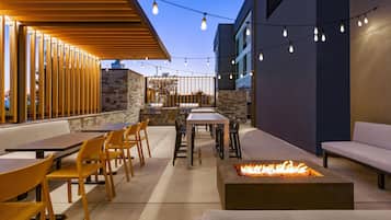 An outdoor patio area with tables and chairs, a fire pit, and string lights.