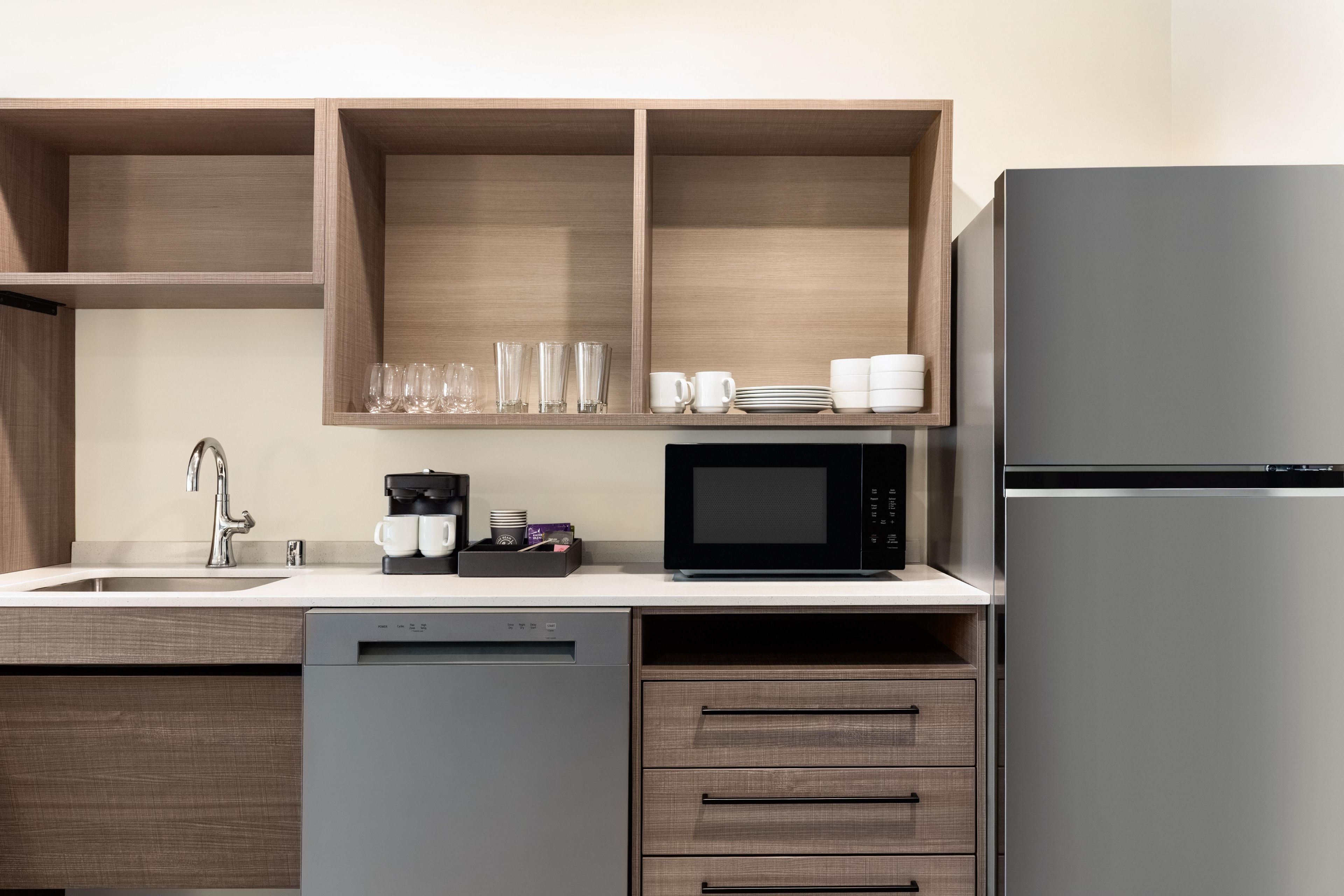 A modern kitchen with a dishwasher, a coffee maker, a microwave, and a refrigerator.