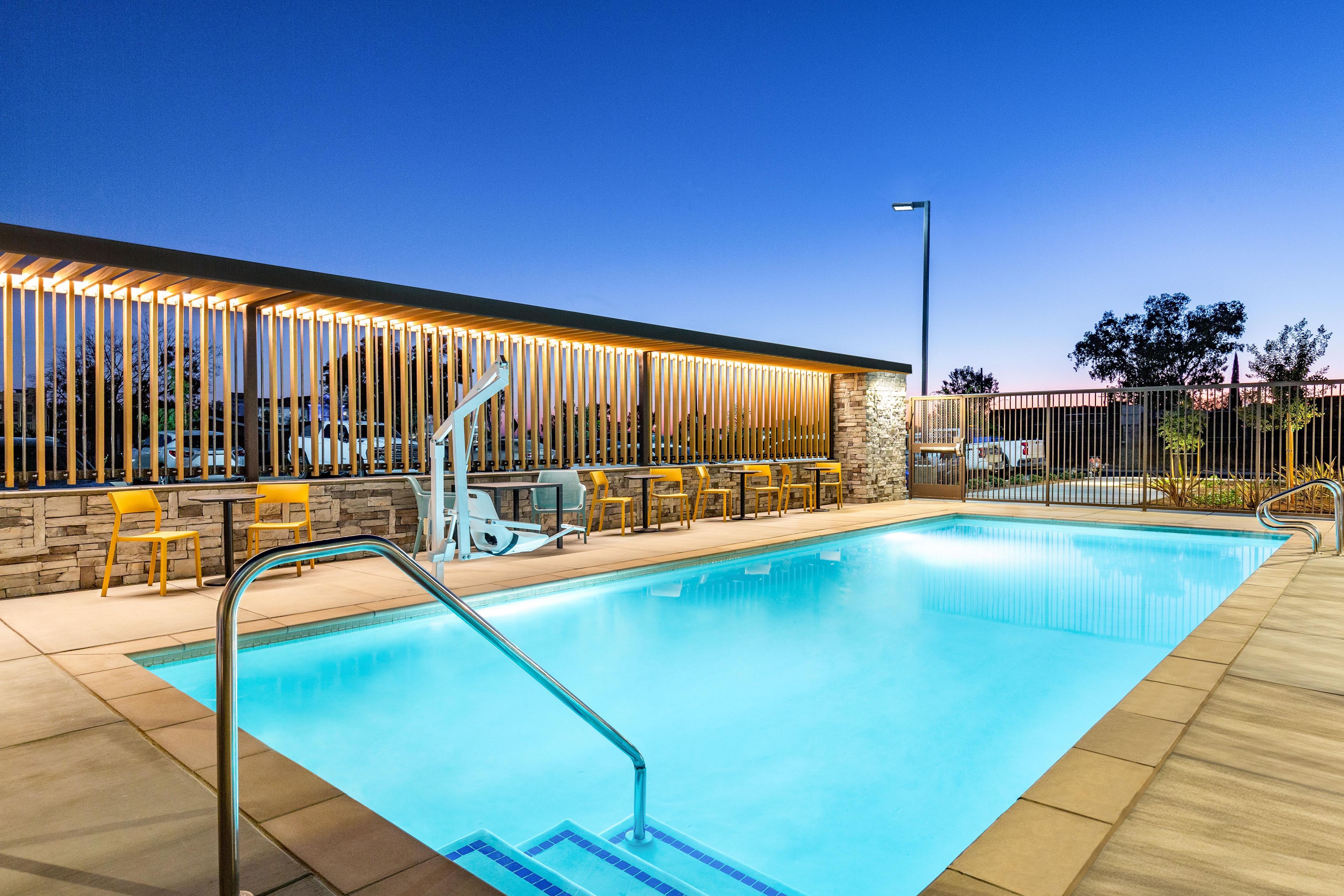 Una piscina con cubierta de madera, pared de piedra y zona de estar al aire libre con sillas y mesas.