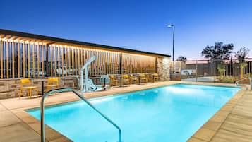 Una piscina con cubierta de madera, pared de piedra y zona de estar al aire libre con sillas y mesas.