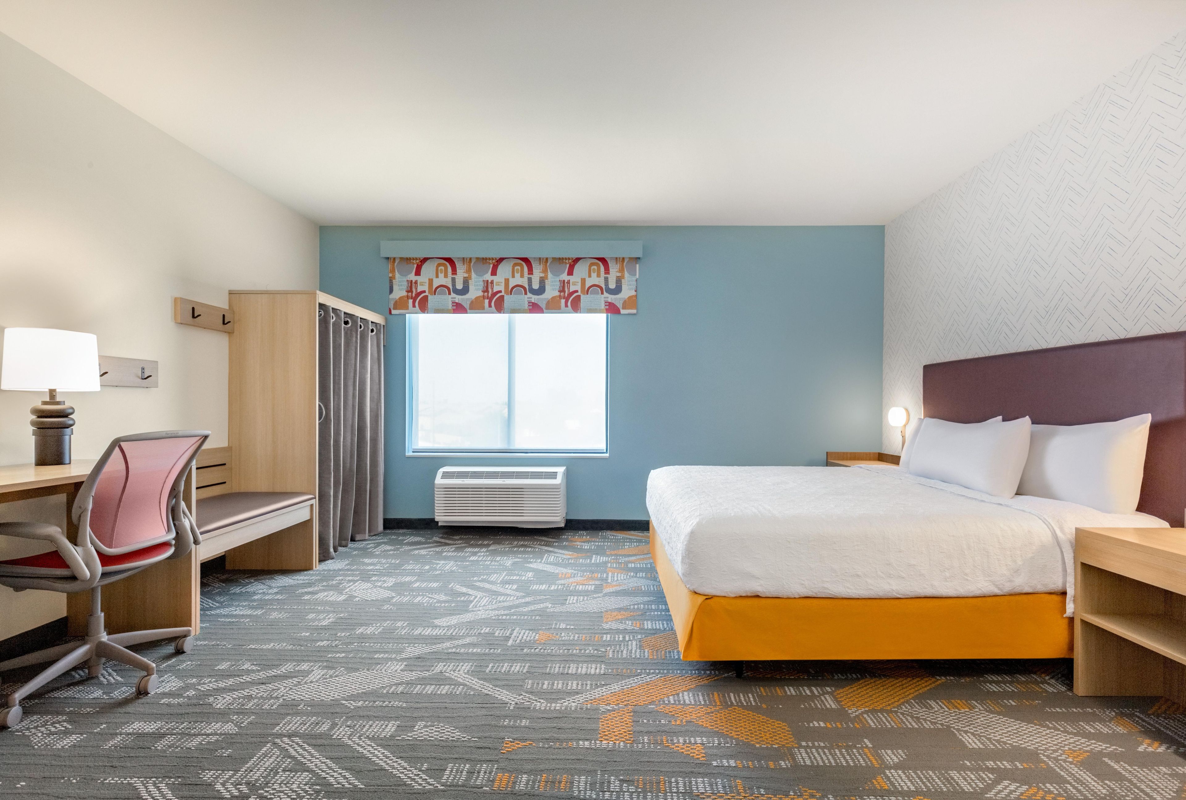 A hotel room with a bed, desk, chair, and a window with curtains.