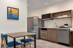 Une cuisine moderne équipée d’un réfrigérateur, d’un four à micro-ondes et d’une machine à café. On y trouve une table à manger avec deux chaises, ainsi qu’un tableau accroché au mur.