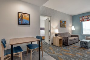 Ett hotellrum med ett matbord, två stolar, en soffa, en lampa och en mönstrad matta.