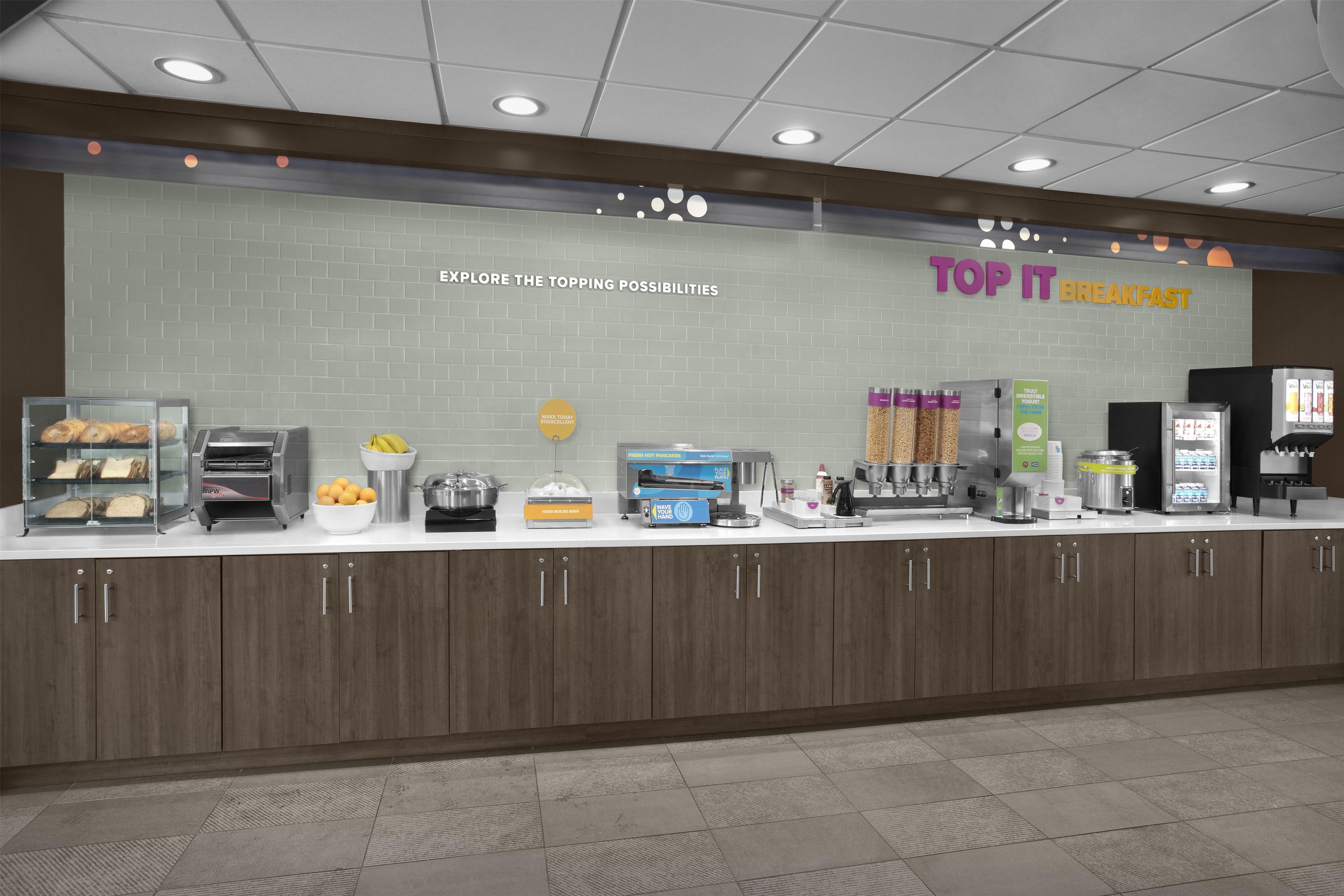 Un comptoir où l’on prend le petit-déjeuner, avec une pancarte indiquant « TOP IT BREAKFAST » et un tableau affichant le menu au-dessus.
