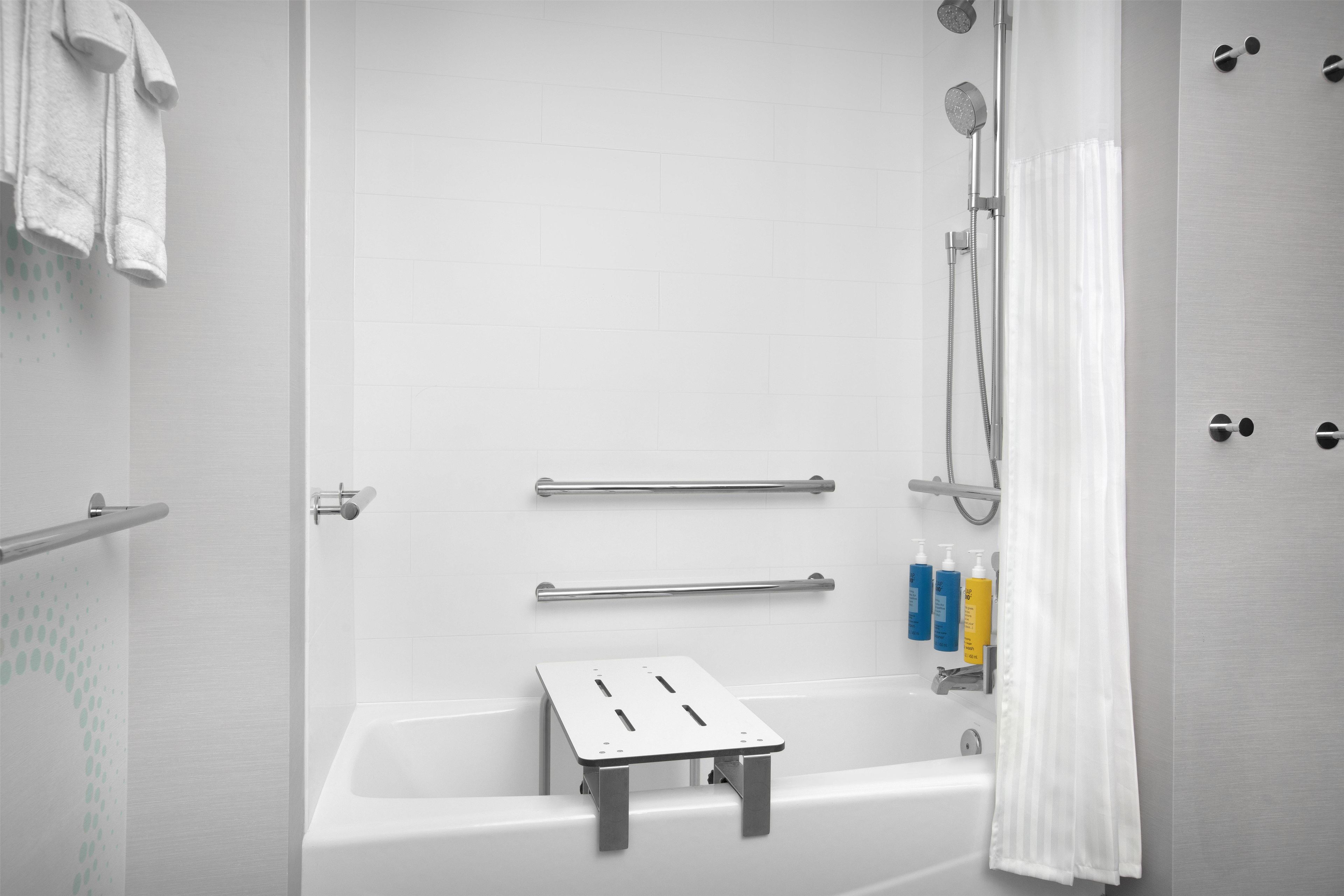 Ett modernt badrum med badkar, dusch, stödhandtag och hygienartiklar.