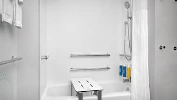 Ett modernt badrum med badkar, dusch, stödhandtag och hygienartiklar.