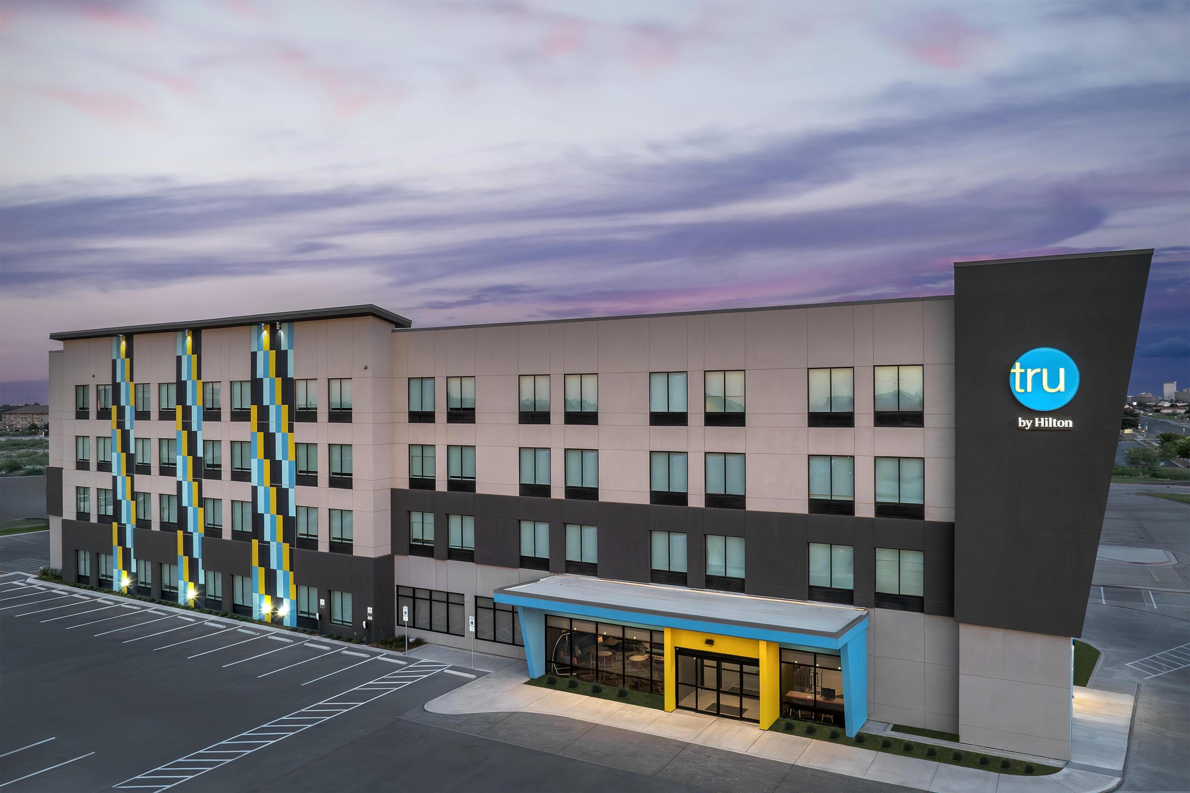 A modern hotel building with a flat roof, multiple windows, and a prominent logo.