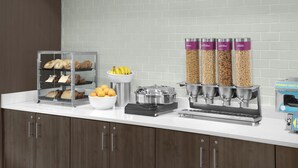 A breakfast bar with bread, fruit, and cereal dispensers. - Tru By Hilton Midland East (Midland)