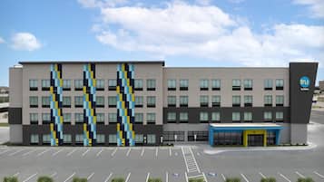 A modern building with a parking lot, a blue entrance canopy, and a logo on the side.