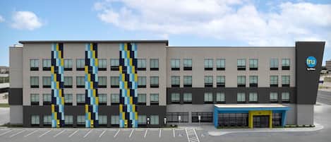 A modern building with a parking lot, a blue entrance canopy, and a logo on the side.