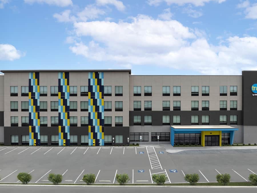 Un bâtiment moderne doté d’un parking, d’un auvent bleu à l’entrée et d’un logo sur le côté.