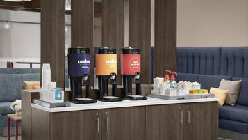 A coffee station with three coffee makers, a water dispenser, and a snack bar with various items.