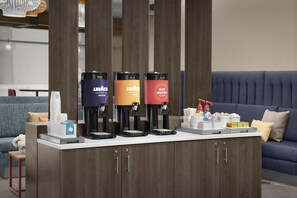A coffee station with three coffee makers, a water dispenser, and a snack bar with various items. - Tru By Hilton Midland East (Midland)
