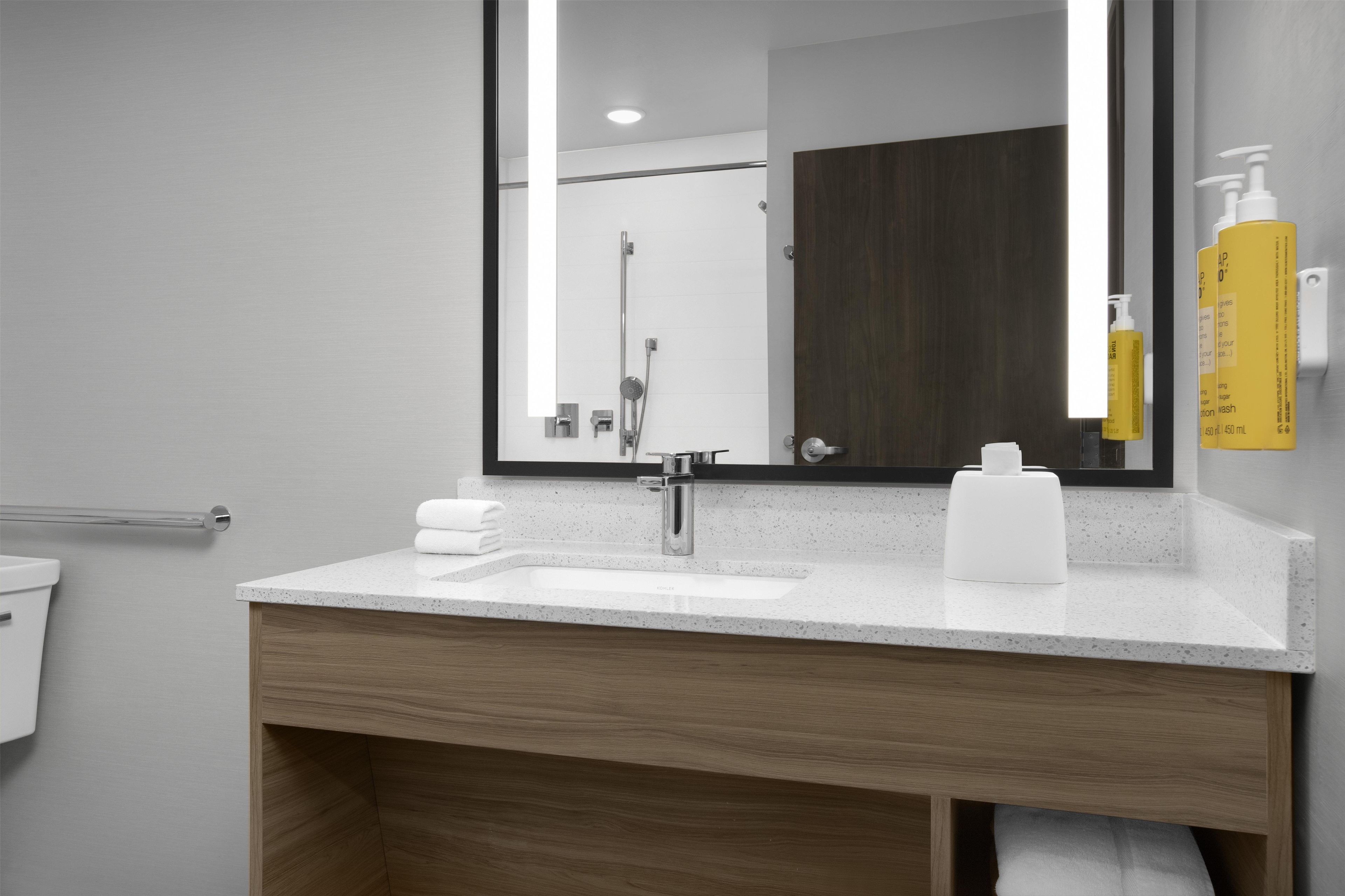 Un baño moderno con un lavabo blanco, tocador de madera, un espejo grande y una ducha.