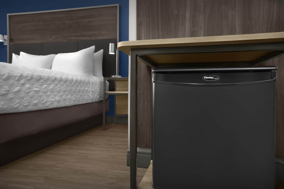 A modern hotel room with a bed, a nightstand, and a built-in mini-fridge.