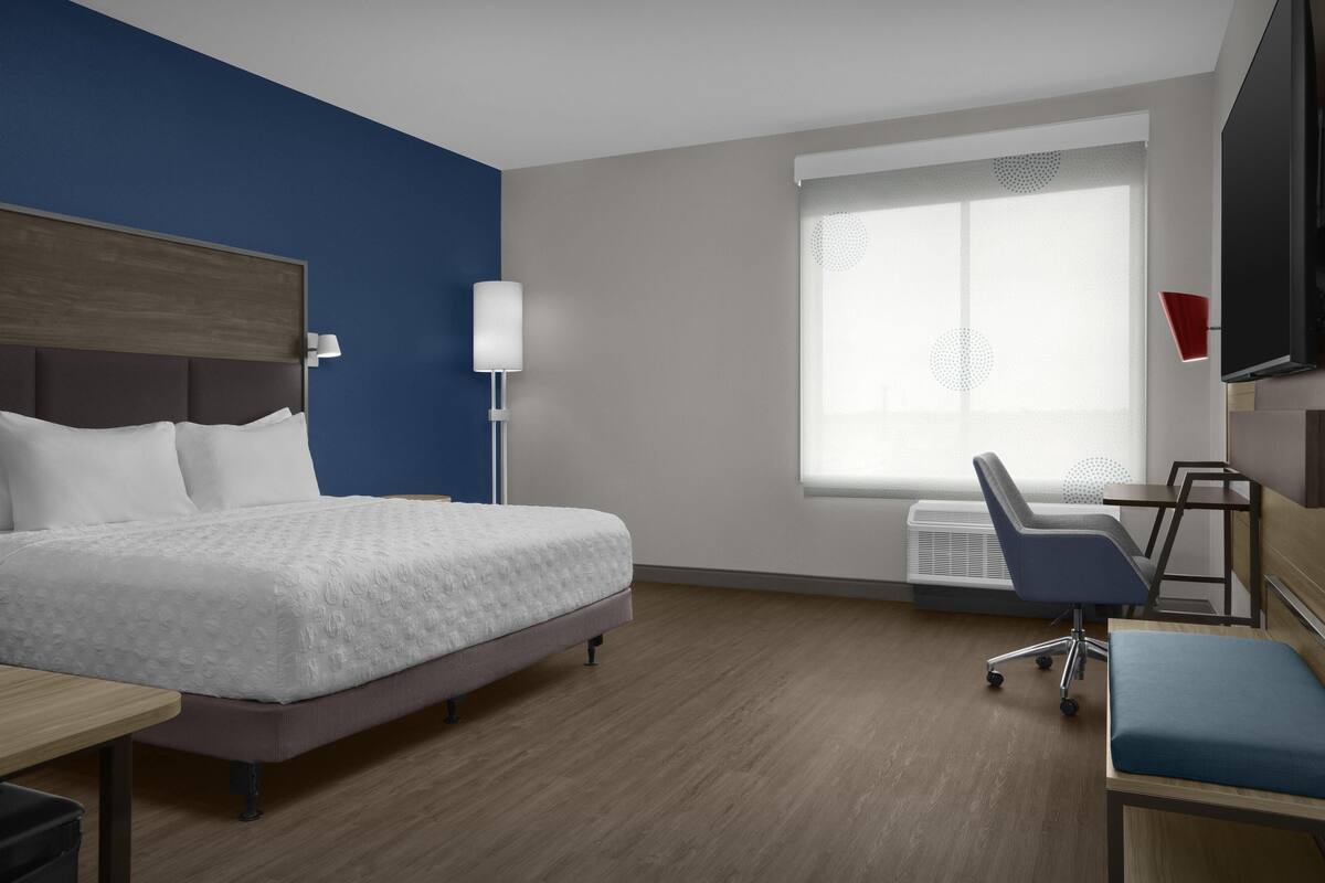 A hotel room with a bed, a desk, a chair, a TV, and a window with blinds.