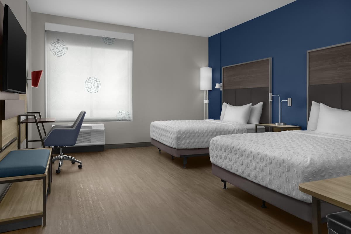 A hotel room with two beds, a desk, a chair, a TV, and a window with a curtain.