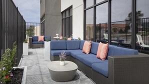 An outdoor seating area with a blue sofa, a round table, and a potted plant. - Tru By Hilton Midland East (Midland)