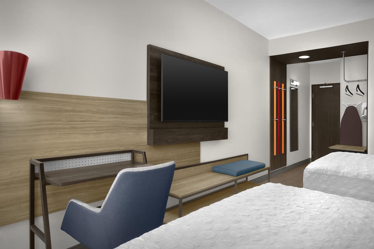 A modern hotel room with a flat-screen TV, a wooden headboard, a bench, a blue chair, and a bed with white bedding.