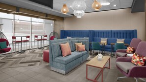 A modern lounge area with a blue sofa, red chairs, a wooden coffee table, and hanging pendant lights. - Tru By Hilton Midland East (Midland)