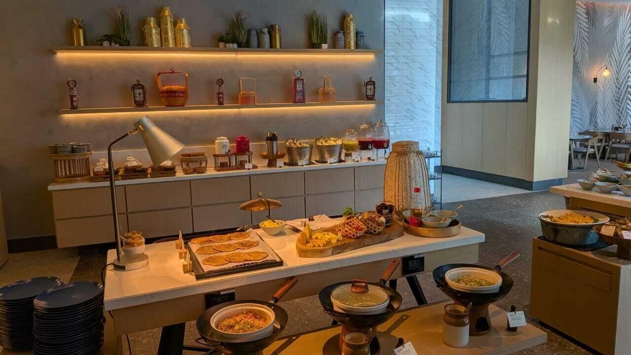 A buffet setup with various food items and kitchenware, a lamp, and shelves with decorative items.