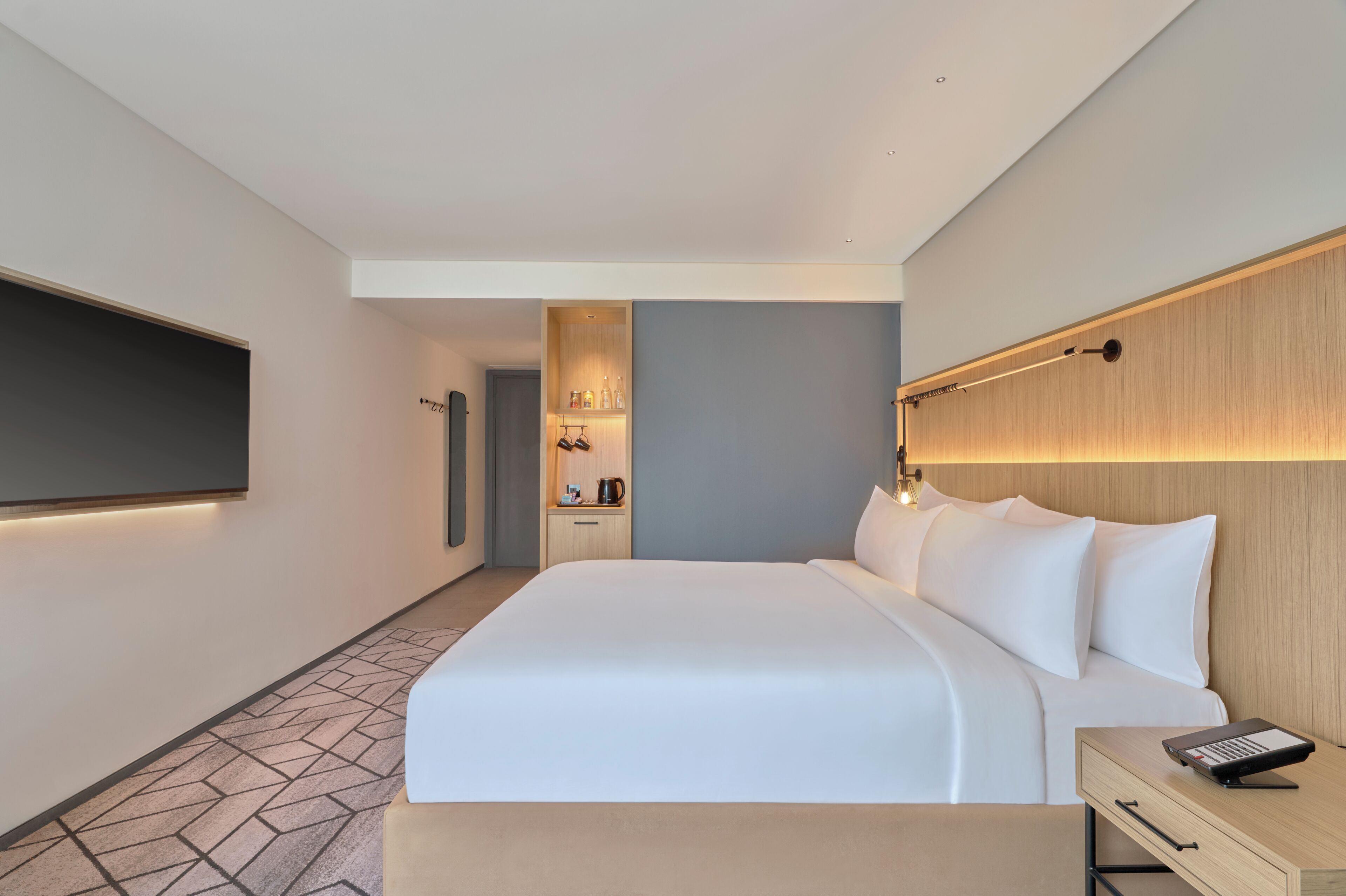 Quarto de hotel moderno com cama grande, mesa de cabeceira e TV de tela plana na parede.