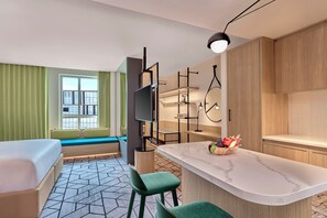 A modern hotel room with a bed, a seating area by the window, a kitchen with a marble countertop, and a TV. - Hilton Garden Inn Bengaluru Embassy TechVillage Outer Ring Road (Bengaluru)