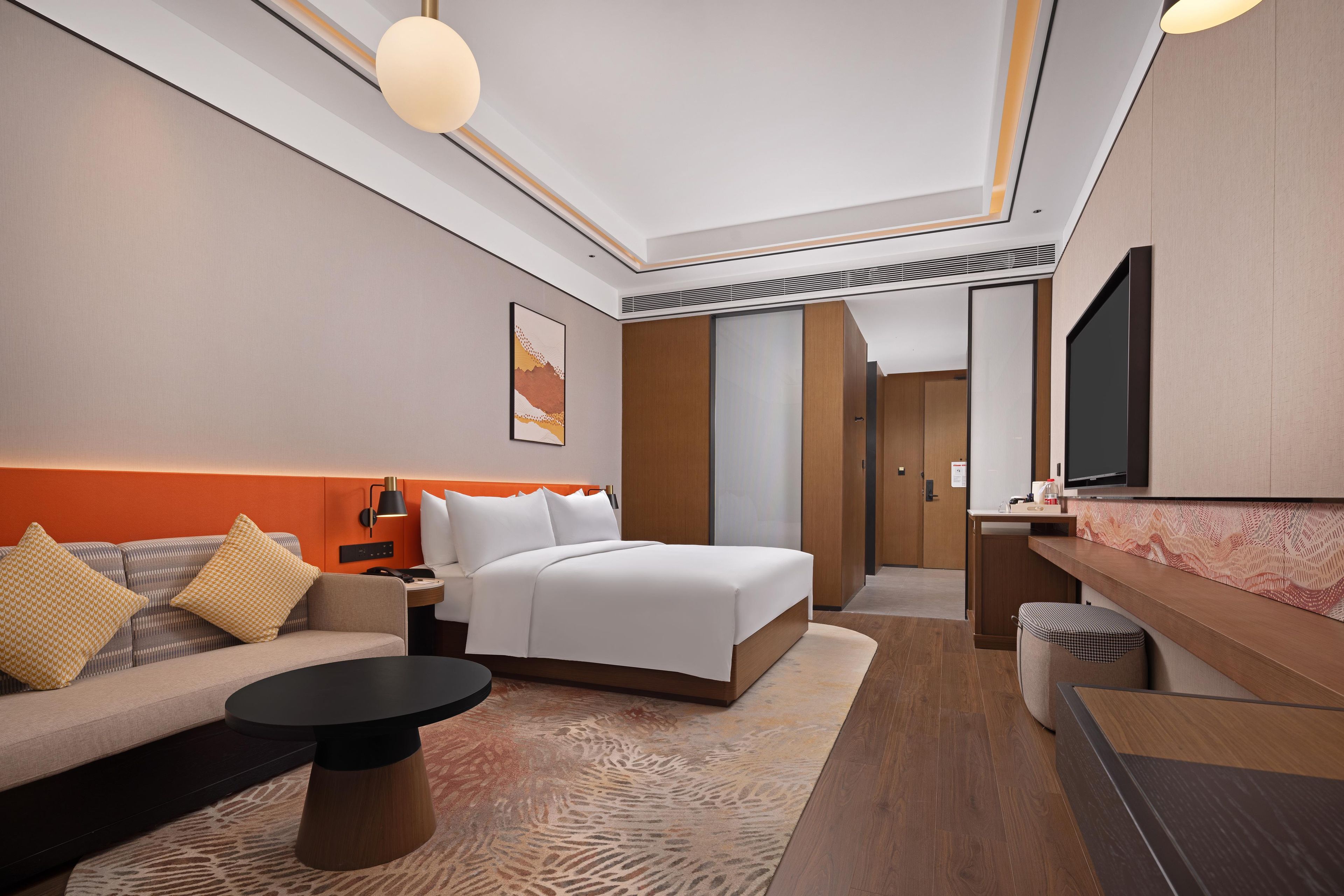 A modern hotel room with a bed, sofa, and a desk area.