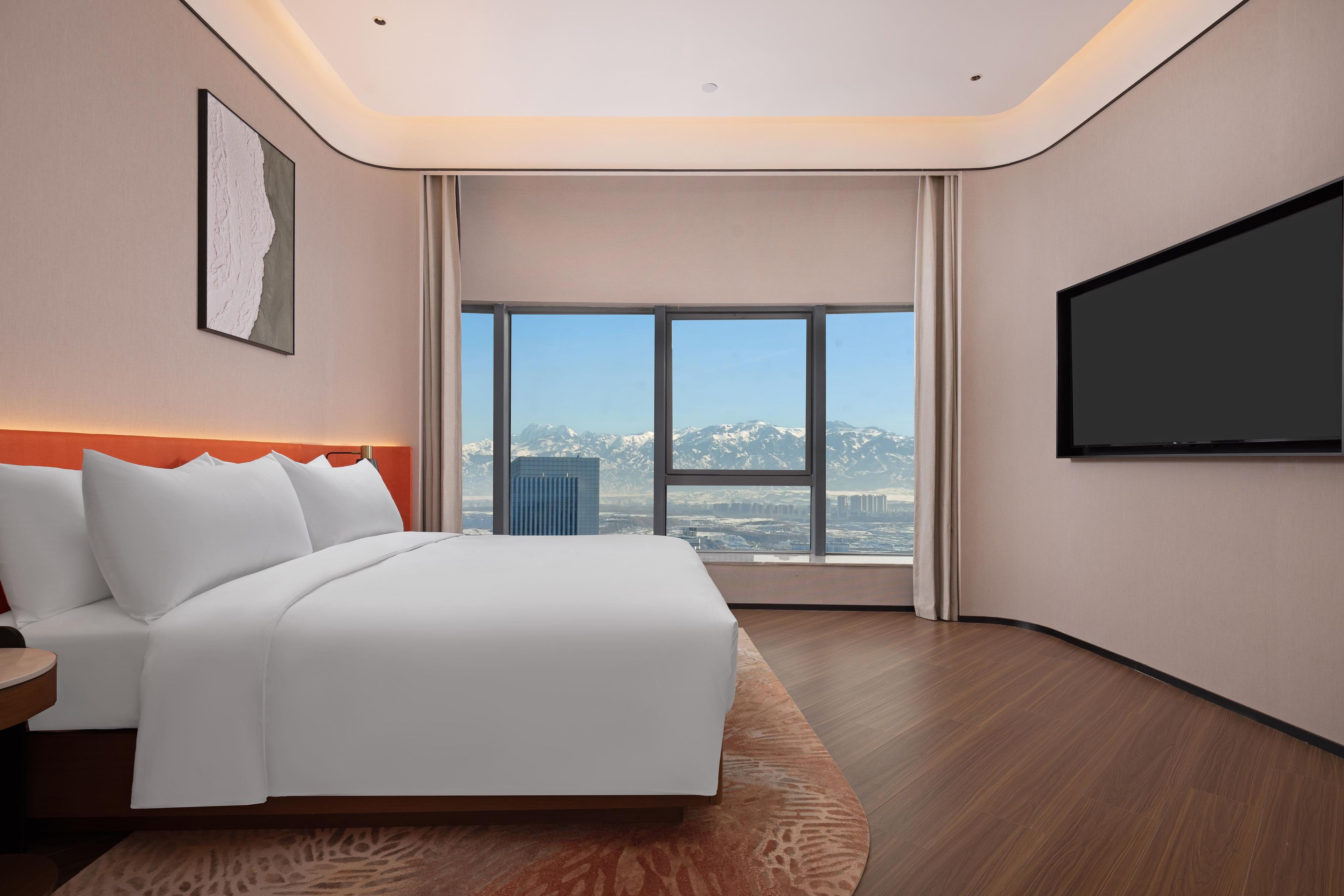 A modern hotel room with a large bed, a flat-screen TV, and a view of a cityscape through large windows.