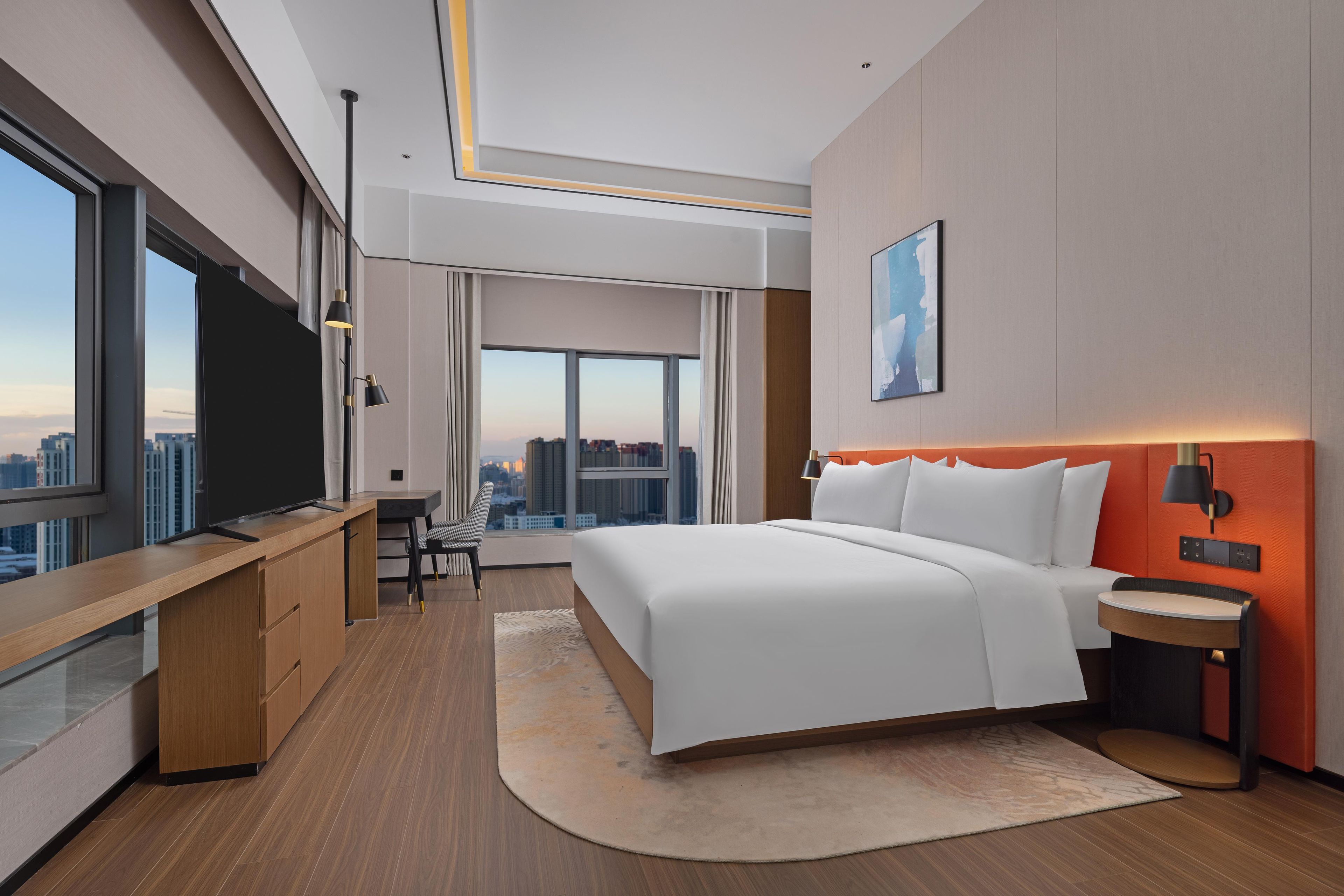 A modern hotel room with a large bed, a desk, a chair, and a view of the cityscape.