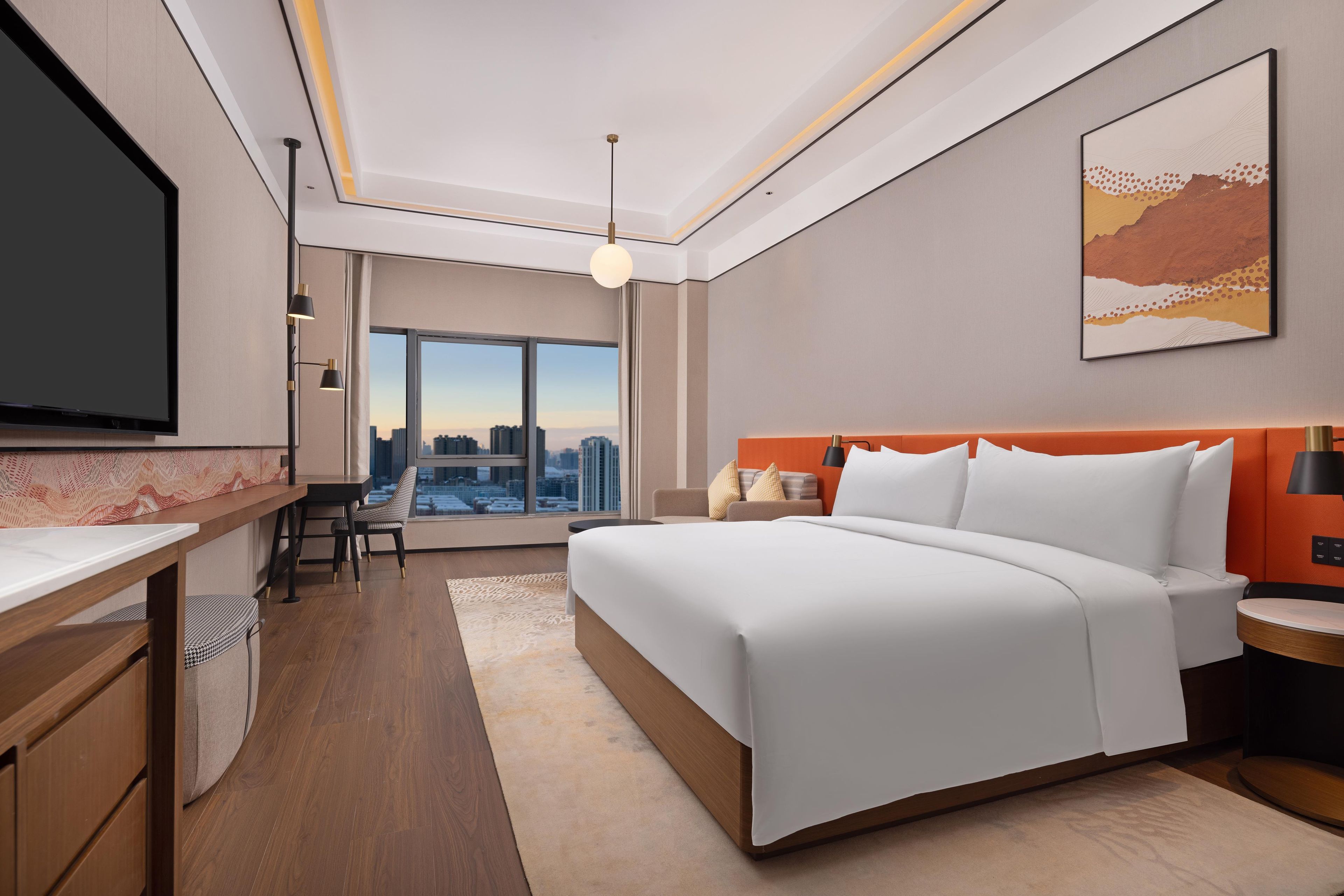 A modern hotel room with a large bed, a desk, and a view of the cityscape.