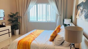 Ein Hotelzimmer mit Bett, Schreibtisch, Lampe und einem fensterbepflanzten Fenster.