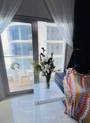 Ein modernes Wohnzimmer mit einem Glastisch, einer farbenfrohen Webdecke und einer Vase mit Blumen.