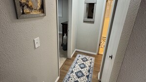 Un couloir avec un tapis à motifs, un tableau et une porte donnant sur une autre pièce.