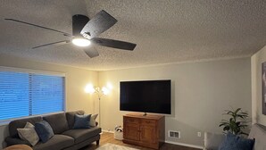 Un salon avec un ventilateur de plafond, deux canapés, un téléviseur et un meuble en bois.