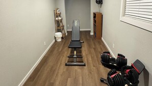 Une salle de sport à domicile équipée d’un banc, d’haltères et d’un ventilateur.