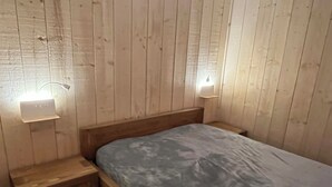 A wooden-paneled room with a bed, a nightstand, and two wall-mounted lights.