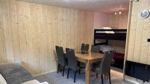 A compact room with a wooden bunk bed, a dining table with chairs, and a sofa.