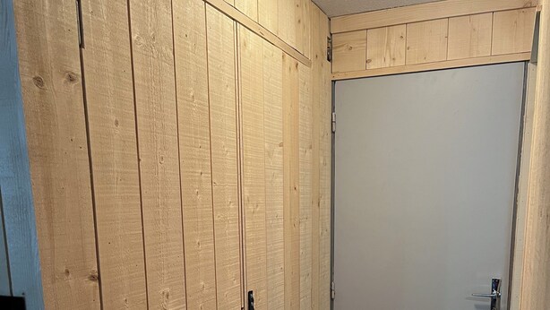 A hallway with wooden paneling, a white door, and a black doormat.