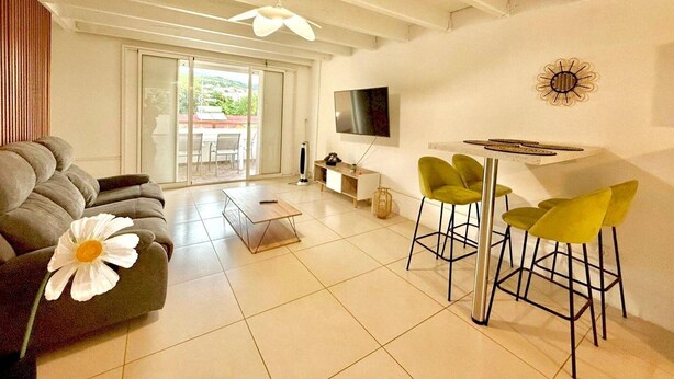 A modern living room with a sofa, a coffee table, a TV, and a dining area with chairs. - La Kaz Pêcheur, Calm (La Possession)