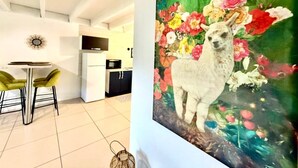 A modern kitchen with white cabinets, a dining area with yellow chairs, and a large painting of a llama with flowers. - La Kaz Pêcheur, Calm (La Possession)