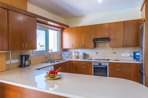 A modern kitchen with wooden cabinets, a large island, a coffee maker, a kettle, and a dishwasher. - Villa Chrystalla by Villa Plus (Poli Crysochous)