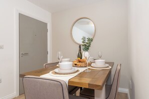 Una mesa de comedor dispuesta con platos, tazones y vasos blancos, una botella y una cesta de cruasanes.