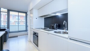 Una cocina moderna con armarios blancos, encimera negra, horno empotrado y ventana con persianas.